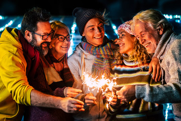 Caucasian happy family enjoy and celebrate by night with fire sparkler all together having fun - christmas and new year eve celebration for group of cheerful people mixed ages and generations