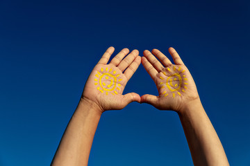 mens two palms with paint yellow sun with smile against blue sky, copy space