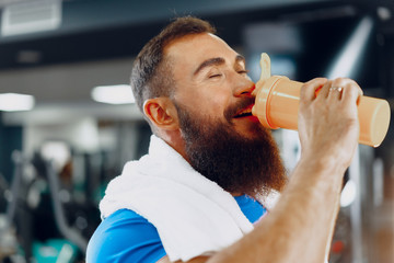 Naklejka na ściany i meble Bearded man bodybuilder having a drink after workout in a gym