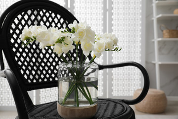 Beautiful white freesia flowers in vase on armchair indoors