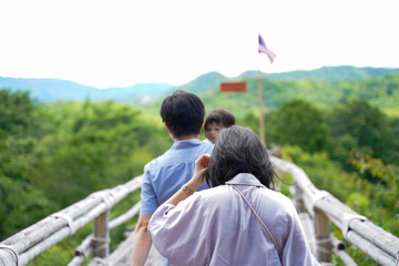 Back view of Young Asian Family with baby on blur backgroundd of top beautiful view of rainforest ,Parents and children while walking on the bamboo bridge with sunlight in morning in Thailand.