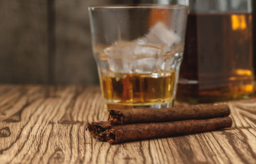 Glass of whiskey and rolled cigars on wooden table