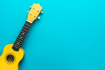 Top view of ukulele with copy space. Yellow colored wooden ukulele guitar on the turquoise blue background. - obrazy, fototapety, plakaty