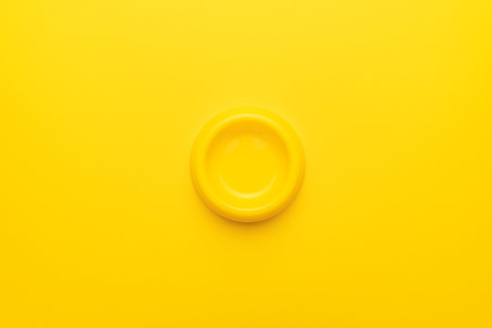 Minimalist photo of yellow pet bowl on the yellow background. Overhead image of empty cat bowl.