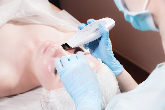 A professional beautician makes an ultrasonic face cleaning to a client in a beauty salon