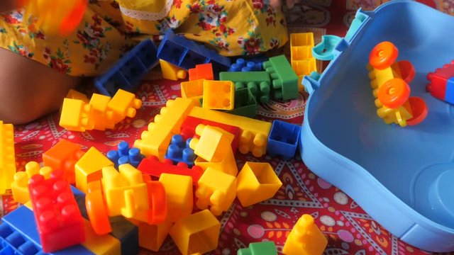Close up of baby child playing with colorful building blocks on bed 