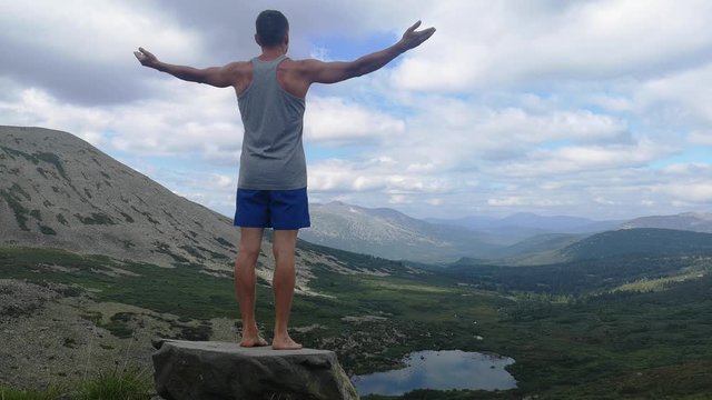 man stands on top of a mountain with open hands. at the top of the mountain, a man with his arms spread wide.