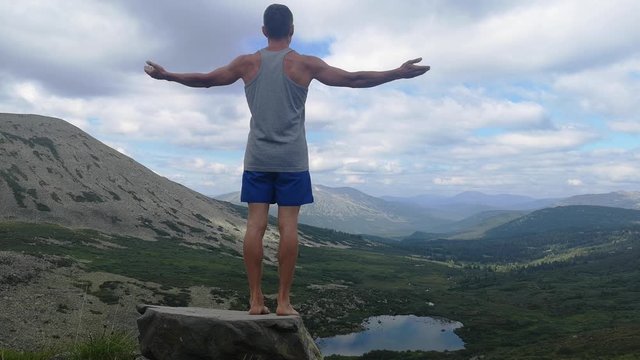 man stands on top of a mountain with open hands. at the top of the mountain, a man with his arms spread wide.