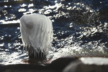 Beautiful ice cap on a sunken tree trunk, sticking out of the water, on the bank of a freezing lake in winter, close-up.