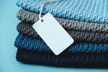 Stack of knitted material from threads of dark blue, light blue, gray colors with blank Price Tag on a blue background. Copy, empty space for text