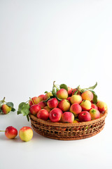 Fototapeta na wymiar Red and yellow ripe apples with leaves in a wicker basket. vertical orientation. No people