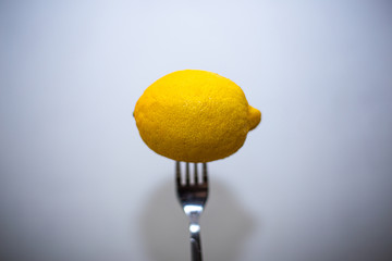 Whole lemon on top on a fork on a white wall background