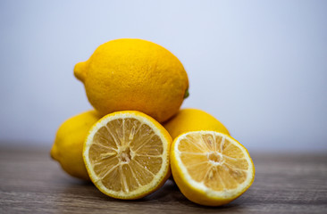 Three whole lemons lie on top of each other, in the foreground two halves of a sliced fourth lemon overall