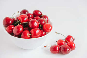 Fresh juicy red cherries in a white plate on the white wooden background. Copy, empty space for text