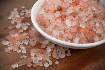 Fototapeta na wymiar Himalayan pink salt in white bowl on wooden table close up