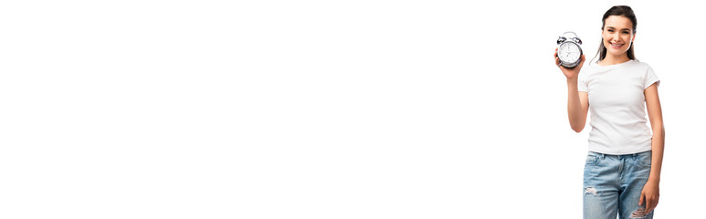 panoramic crop of brunette woman in white t-shirt and jeans holding retro alarm clock isolated on white