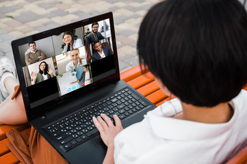 Fototapeta na wymiar Online learning. Back view of a young girl, student with a laptop. The girl learns online using a laptop by a video conference. On the laptop screen, the teacher teaching his students