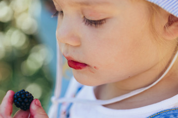 Close-up shot of a cute little girl with ripe blackberry in her fingers and lips, colored in purple color by berry juice. Natural nutrition and vitamin concept.