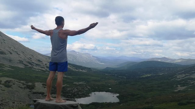 man stands on top of a mountain with open hands. at the top of the mountain, a man with his arms spread wide.