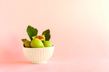 Ripe yellow fig fruit with leaf in a white ceramic bowl on light pastel background. Harvest and healthy eating concept. Selective focus