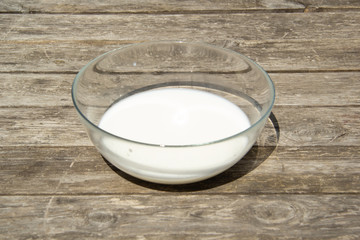 Milk in a glass bowl is measured for the preparation of yeast dough. The glass salad bowl stands on a wooden surface. Cooking pizza at home