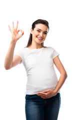 pregnant woman in white t-shirt touching belly and showing ok sign isolated on white