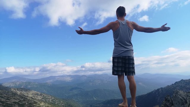 man stands on top of a mountain with open hands. at the top of the mountain, a man with his arms spread wide.