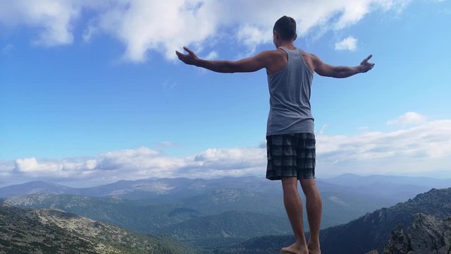man stands on top of a mountain with open hands. at the top of the mountain, a man with his arms spread wide.