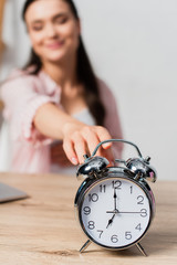 selective focus of brunette woman reaching retro alarm clock