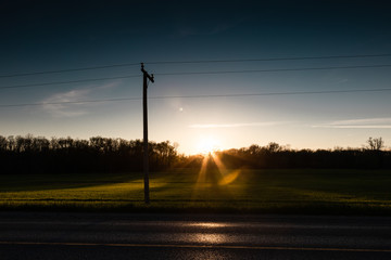 Moody country road at sunset with power lines in the foreground.