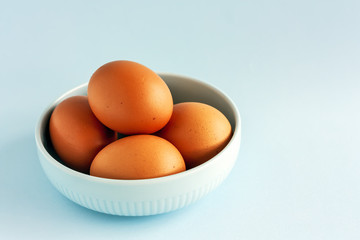 Fresh organic raw eggs in blue bowl on light pastel background. Healthy breakfast and fresh ingredients. Selective focus