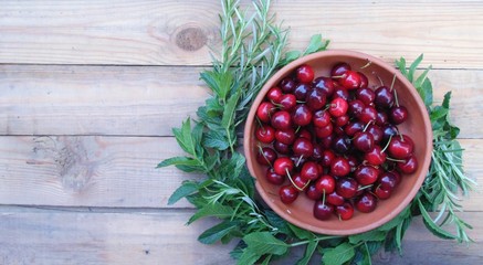 Red cherry berries in a ceramic plate. Rosemary and mint are next to the plate. Against the background of a wooden table. Space for text.
