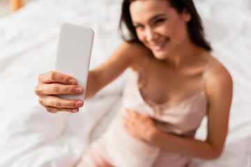 selective focus of pregnant woman taking selfie in bedroom