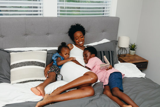 Black Mother And Her Children Embracing And Cuddled In Bed At Home