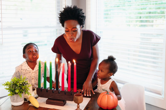 Black mother blowing out Kwanza candles with children 