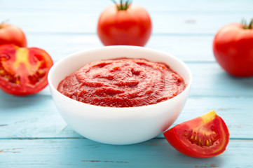 Tomato ketchup sauce in a bowl with tomatoes on blue wooden background. View from above.
