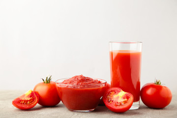Fresh tomatoes with paste and juice on grey background