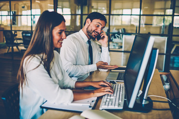 Male manager talking on phone about project while his female colleague typing on computer, professional employees busy during working process using modern technologies for searching information