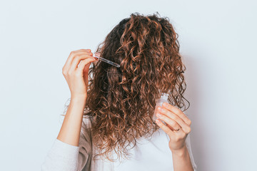 Woman applying cosmetic oil to her beautiful curly hair