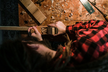 Mann mit Dreadlocks in rotem Hemd hobelt ein Stück Holz von oben aufgenommen