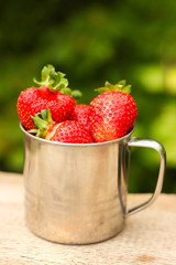 juicy ripe strawberries in a metal mug on an old wooden table in rustic style in the garden