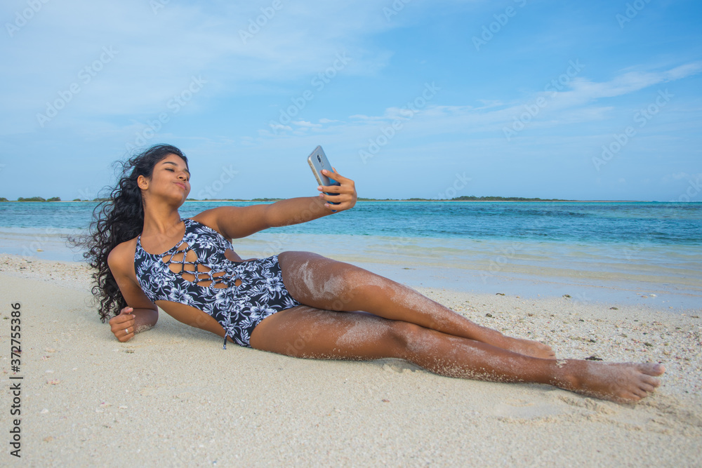 Wall mural Young black woman taking a selfie lying at beach