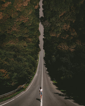 A young lady standing on a countryside asphalt road. Photo in the style of the film Inception. Droneception.