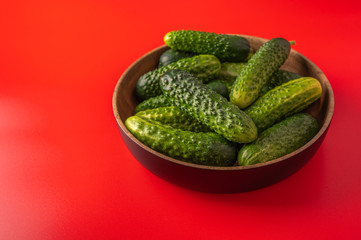 Fresh cucumbers in a bamboo bowl on a red background, selective focus, copy space, close up