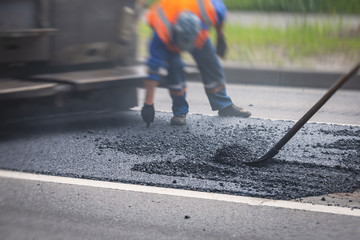 Asphalt paver machine and steam road roller during road construction and repairing works, process of asphalting and paving, workers working on the new road construction site, placing a layer