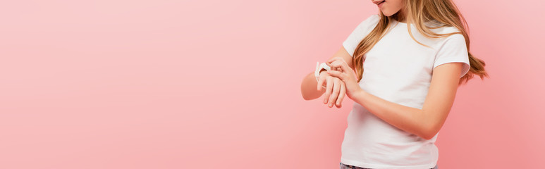 partial view of child in white t-shirt touching smartwatch isolated on pink, panoramic concept