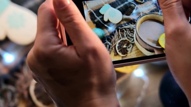 Female hands take pictures a cup of cocoa on the background of a garland. A woman photographs food in a cafe. New Year theme. 2021