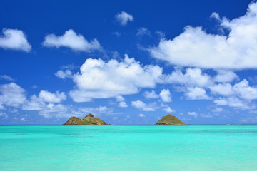 Tropical Hawaiian beach with picturesque turquoise waters, puffy clouds, and clear blue skies view of Mokuluas at Lanikai in Kailua, Oahu
