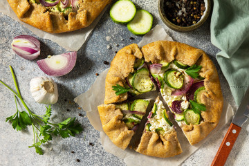 Healthy pastries made from rye flour, dessert diet food. Galette with zucchini, onions and feta on a light stone table. Top view flat lay background.