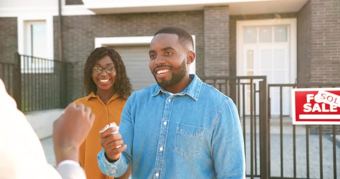 Rear of real-estate selling house to African American happy couple and handing keys. Outdoor. Joyful married man and woman hugging and buying home at outskirt. Getting dwelling in suburb. back view.